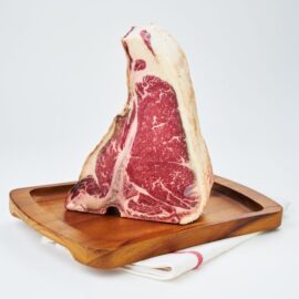 A thick-cut, beautifully marbled 45 Days Dry Aged Barley Fed T-Bone Steak MS3+ on a dark surface.