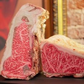 A thick, beautifully marbled Dry-Aged Wagyu Bone-In Striploin steak on a dark surface.