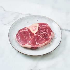 Close-up shot of a perfectly cooked, tender Grass-Fed Beef Osso Bucco in a rich, savory sauce.