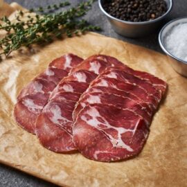 A beautifully marbled, thinly sliced arrangement of Dingley Dell Coppa on a rustic wooden board.