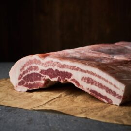 A premium cut of Dingley Dell Pork Belly with skin on, showing distinct layers of rich meat and creamy fat.