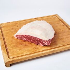 A beautifully marbled Wagyu Rump Cap Steak MS7 with a thick, creamy fat cap, presented on a dark surface.